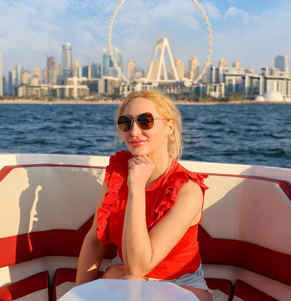 Joelle Monroe on a boat, the Dubai skyline with a Ferris wheel in the background.